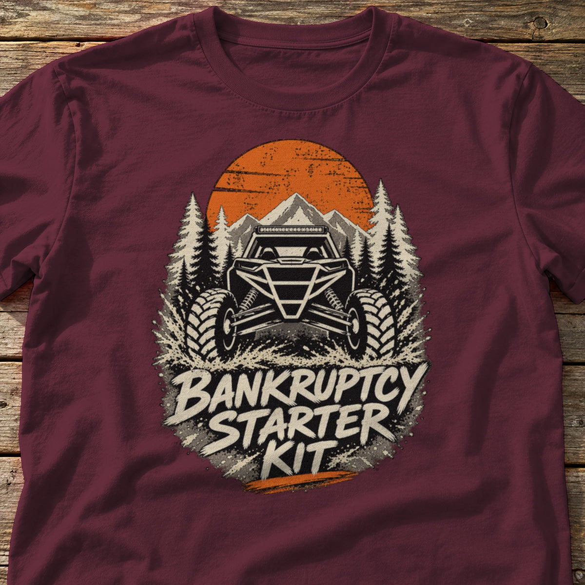 Bankruptcy Starter Kit t-shirt in Maroon, laid flat on weathered wood