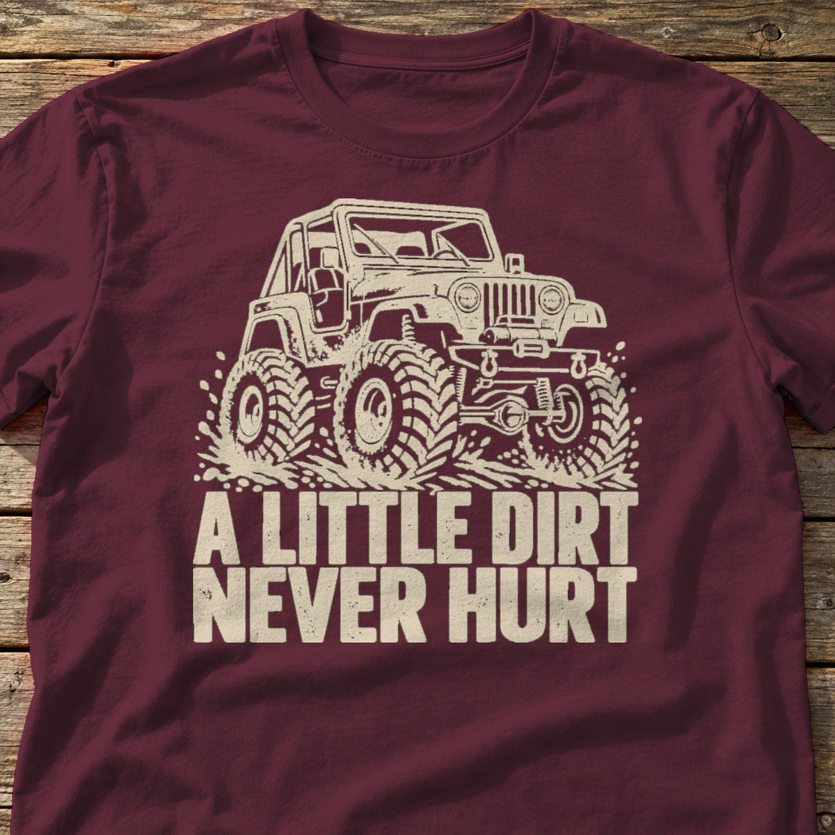 A Little Dirt Never Hurt t-shirt in Maroon, laid flat on weathered wood