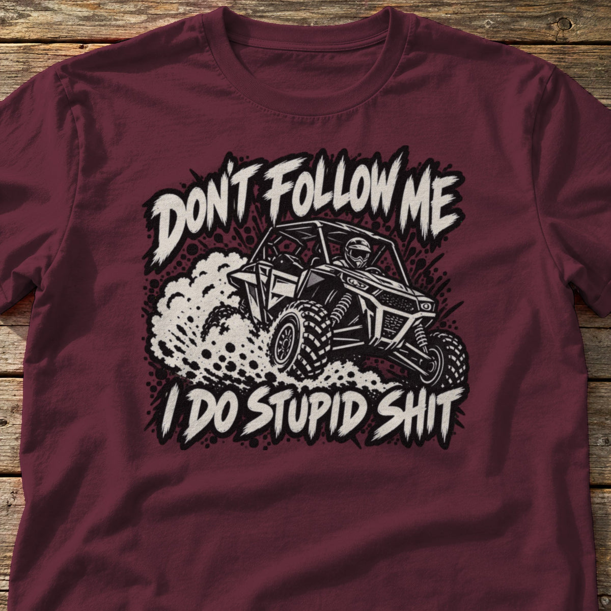 Don't Follow Me I Do Stupid Shit t-shirt in Maroon, laid flat on weathered wood