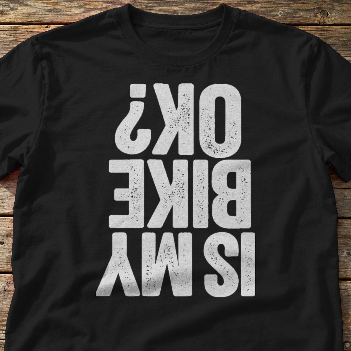 Is My Bike OK? t-shirt in Black, laid flat on weathered wood