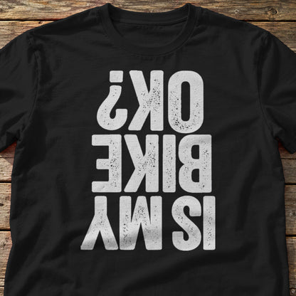 Is My Bike OK? t-shirt in Black, laid flat on weathered wood